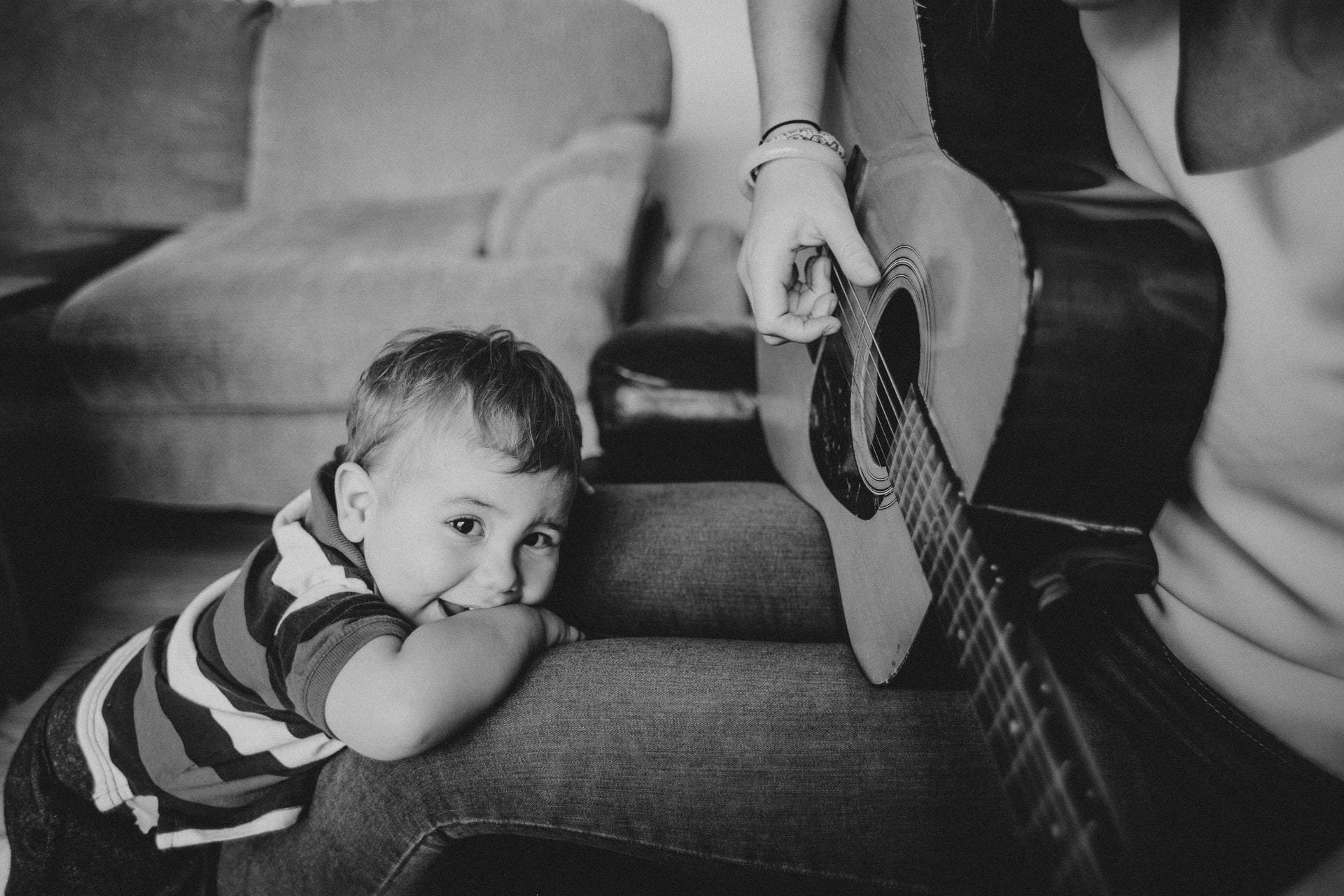 Baby looking at camera while person plays guitar.